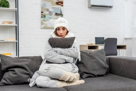 a woman sits on a couch warming up and bundling up